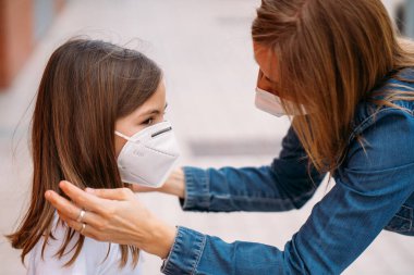 Anne sokakta kızının yüzüne maske takıyor.