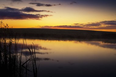 Canlı turuncu gün batımı sakin bir göle yansıyor.