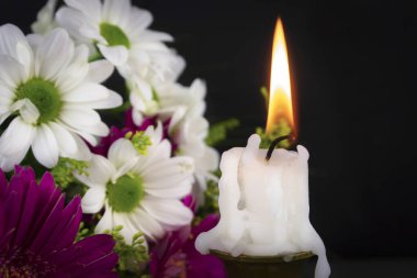 Short candle burning in close-up among flowers clipart