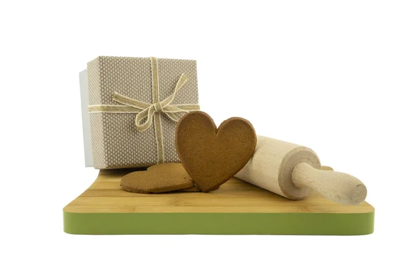 ハート型のクッキープレゼントのコンセプトは ギフトボックスの横に茶色のビスケットと白い背景に隔離された木製のカッティングボード上のローリングピン — ストック写真