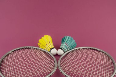 Badminton raketleri ve pembe arka planda mavi ve sarı renkli mekikli horozlar.