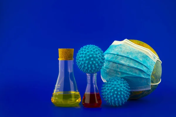 Concept of research for a Covid-19 vaccine with a conical lab flasks with yellow and red solutions alongside a hypodermic syringe and blue virus molecules over a blue background with copy space