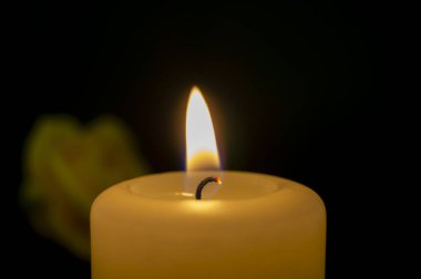 Koyu arkaplanda gülün yanında yanan tek bir sarı mum