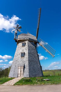 Baharda yemyeşil bir tarlada, güneşli mavi gökyüzüne karşı manzaralı tarihi yel değirmeni.