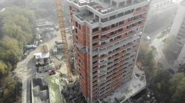 İkamet binasının yanında duran sis içindeki kule vinci kuş bakışı. İnşaat alanının üzerinde uçuyor. İHA gerçek zamanlı görüntüler.