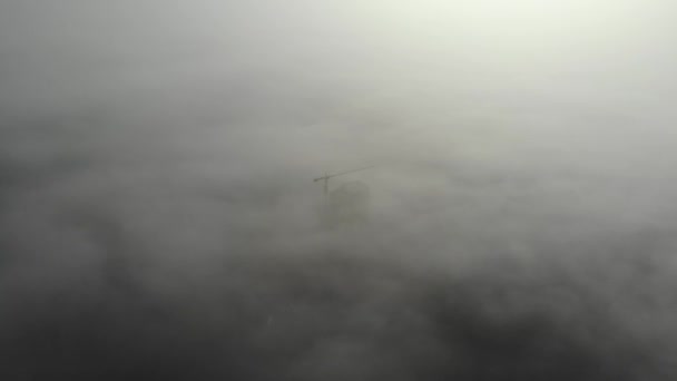 Fågelskådning på tornkran i dimma står bredvid bostadshus. Flyger över byggarbetsplatsen. Drönare realtidsbilder. — Stockvideo