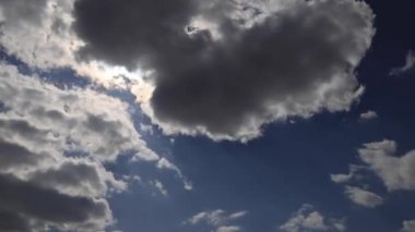 Güzel 4K zaman aşımı. Güneş ışınları parlak mavi gökyüzünde beyaz kabarık bulutları delip geçer.