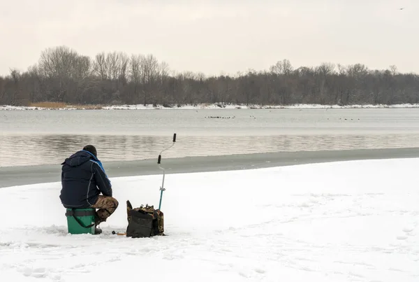 Buz kütlesinde oturan ve delikte balık tutan bir balıkçı.
