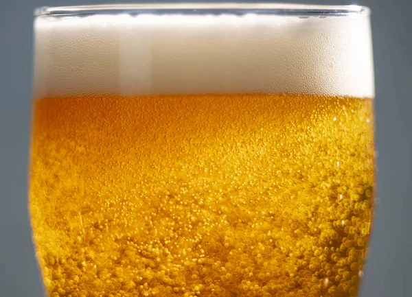 Bolhas e espuma nos raios de luz em um copo de cerveja close-up — Fotografia de Stock