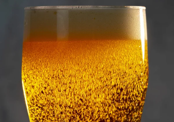 Bolle e schiuma nei raggi di luce in un bicchiere di birra primo piano — Foto Stock