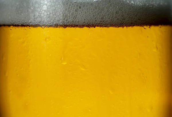 Bolhas e espuma nos raios de luz em um copo de cerveja close-up — Fotografia de Stock