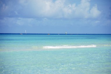 Okyanusun turkuaz sularında bulutlara karşı yelken açan gemiler.