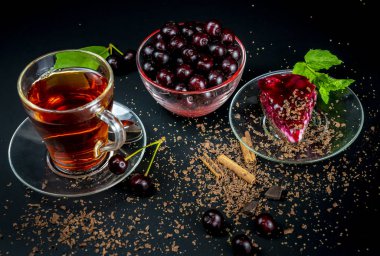 Bir fincan koyu çay, olgun kirazlar ve siyah arka planda vişneli pastayla hayat