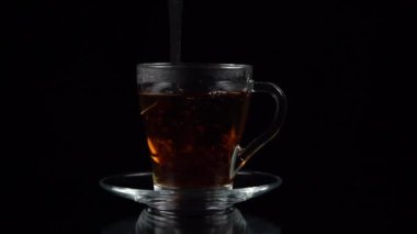 Çay kaşığı çay fincanında çay yaprakları ve siyah arka planda çay tabağı, yavaş çekim.