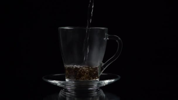 熱湯をグラスティーカップに注ぎ 紅茶の一部を注ぎ ゆっくりとした動き 黒い背景で注ぎます — ストック動画