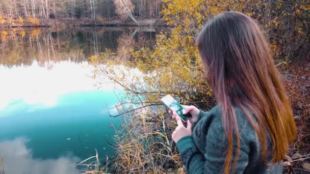 一个女孩 在美丽的森林湖畔 用智能手机在社交网络聊天时写道 — 图库视频影像