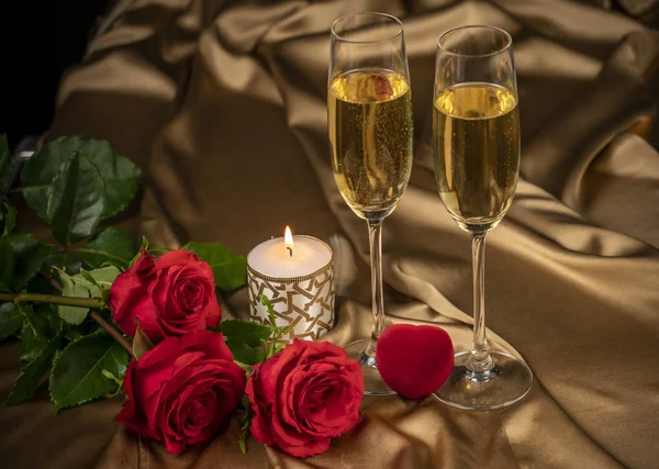 Sevgililer günü kartı, altın arka planda iki kadeh şampanya kırmızı güller ve kırmızı bir kalp, yanan bir mum.