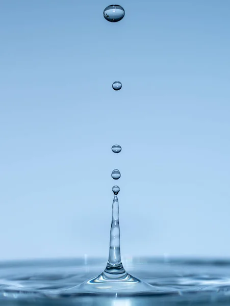 Gotas de água formam ondulações ao cair em água clara azul claro, gotas e salpicos de close-up — Fotografia de Stock