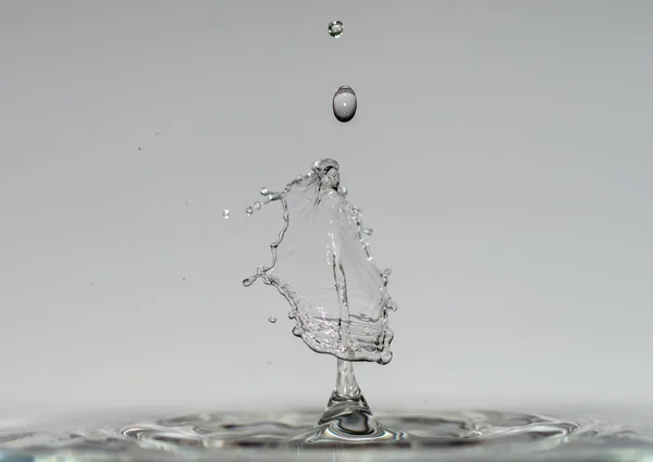 Le gocce d'acqua formano sculture trasparenti ipnotizzanti quando cadono in acqua chiara azzurra, gocce e spruzzi di primo piano — Foto Stock