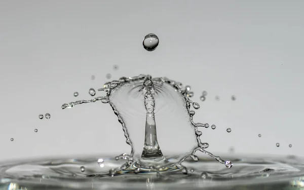 Gotas de agua caen desde una altura de agua pura y clara formando salpicaduras en forma de formas originales de paraguas, setas y coronas —  Fotos de Stock