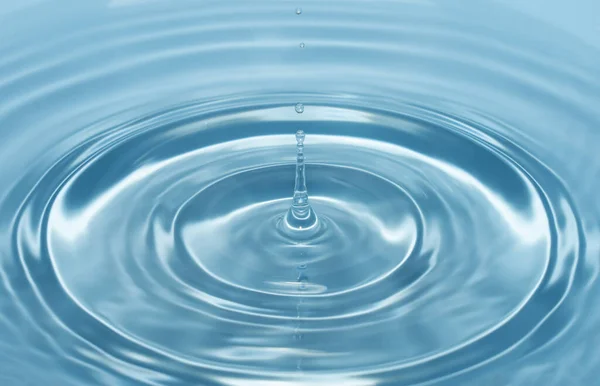 Uma gota de água cai com um respingo na água clara e azul formando círculos na água — Fotografia de Stock