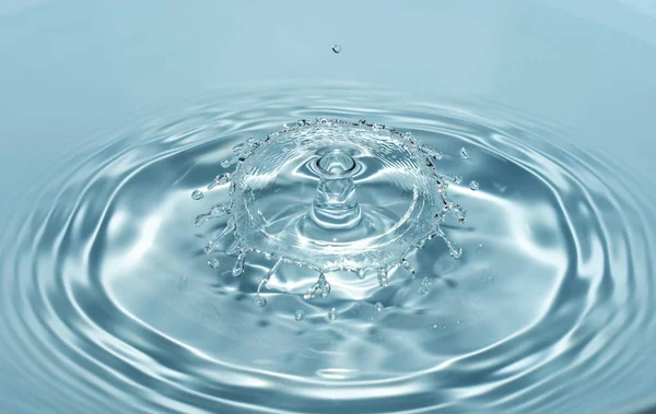 Gotas de agua limpia y dulce caen desde una altura de agua azul transparente formando salpicaduras en forma de figuras originales — Foto de Stock