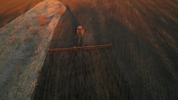 Travaux de terrain de printemps, tracteur cultive la terre à la lumière du coucher du soleil, vidéo aérienne — Video