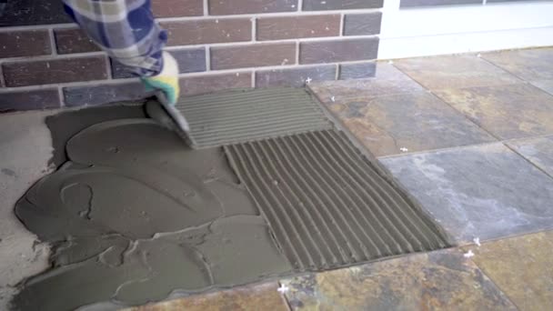 바닥에 세라믹 타일을 깔고 빗으로 타일 접착제를 평준화하는 모습 — 비디오