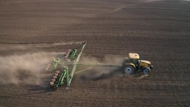 Trabajos de campo de primavera, un tractor con una sembradora montada siembra semillas en el suelo en un campo agrícola — Vídeos de Stock