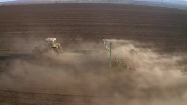 Trabajos de campo de primavera, un tractor con una sembradora montada siembra semillas en el suelo en un campo agrícola — Vídeos de Stock