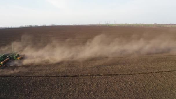 Trabajos de campo de primavera, un tractor con una sembradora montada siembra semillas en el suelo en un campo agrícola — Vídeo de stock