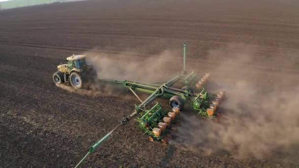 Trabajos de campo de primavera, un tractor con una sembradora montada siembra semillas en el suelo en un campo agrícola — Vídeos de Stock