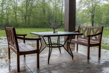 Şiddetli yağmurda verandada iki ahşap bank ve bir masa standı.