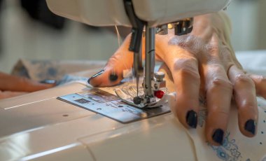 Dikiş makinesinin kenarındaki terzinin ellerine yakın plan kumaş, giysi..