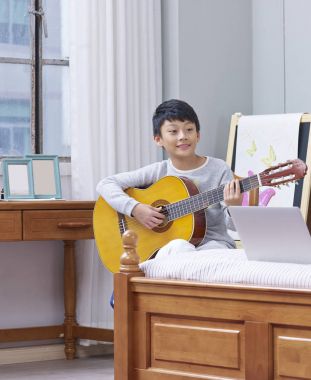 young asian boy practicing guitar at home 