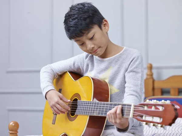 genç Asyalı çocuk öğrenme, pratik ve evde gitar çalma