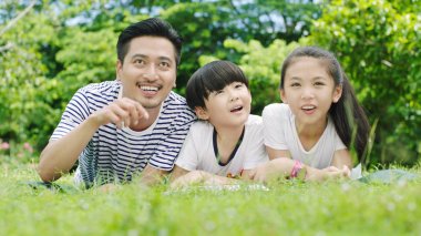 Asya aile ararken ve yüzüstü yatarken gülümseyen ve otlak üzerinde okuma