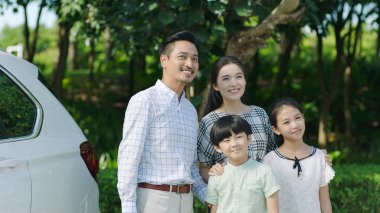 Asian family standing beside car looking forward and smiling clipart