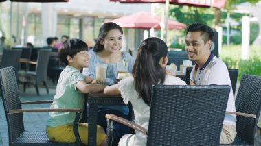 Asian family smiling, eating & drinking outdoor at streetside table clipart