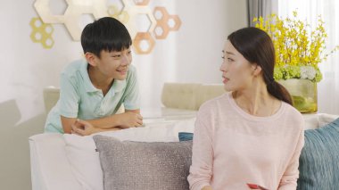 Asya genç çocuk gülümseyen ve kapalı evde annesiyle konuşuyor