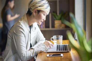 Akıllı telefon ve dizüstü kahve dükkanında kullanarak gülümseyen genç Asyalı kadın       