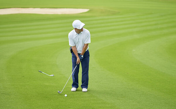 Asian golfer standing in course aiming and preparing for putting
