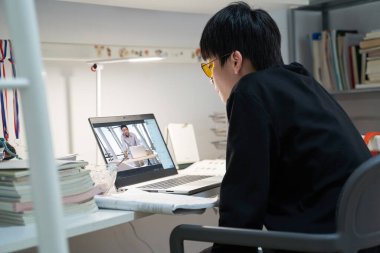 Covid-19 sırasında bilgisayar gözlüğü takan Asyalı bir çocuk evde ders çalışıyor.