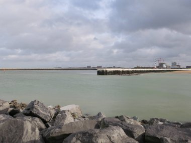 Bulutlu gökyüzü, vinçler ve deniz feneri olan Ostend iskelesi.