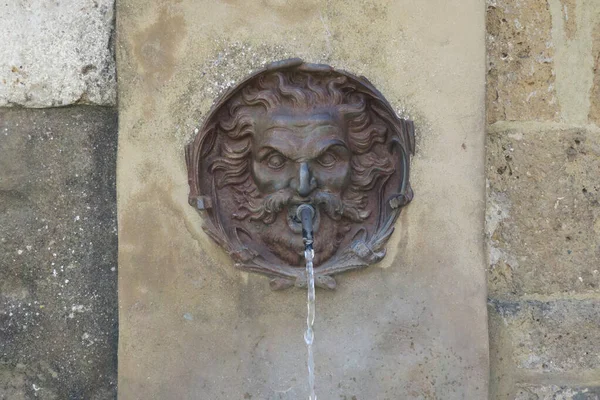 a gargoyle spitting water at a well in Pitigliano