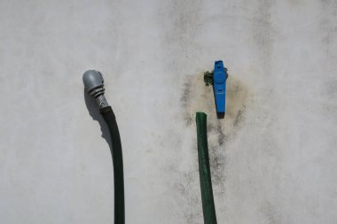 İki tüp ve mavi musluğu olan gri bir duvar.