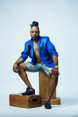 Mavi elbiseli ve mavi dudaklı bir adamın stüdyo portresi