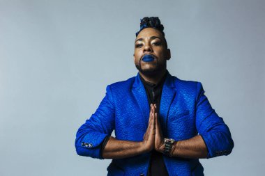 Mavi elbiseli ve mavi dudaklı bir adamın stüdyo portresi. Meditasyon, dua, meditasyon.