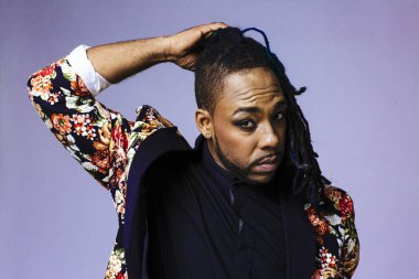 Çiçek desenli bir takım elbise giyen ve saçlarıyla oynayan bir adamın stüdyo portresi.