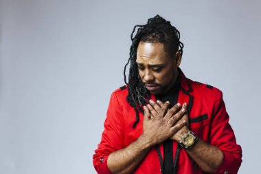 Kapalı stüdyo portresi. Kırmızı ceketli bir adam. İki eli de kalpte.